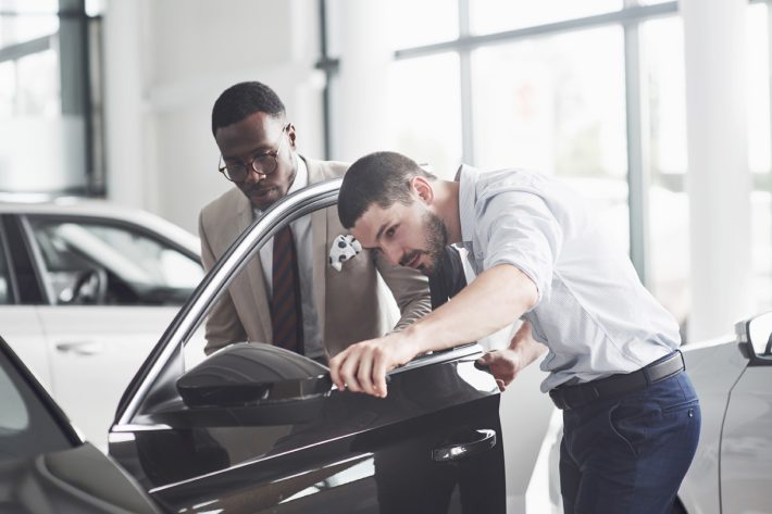 An African man who buys a new car checks a car talking to a professional vendor.